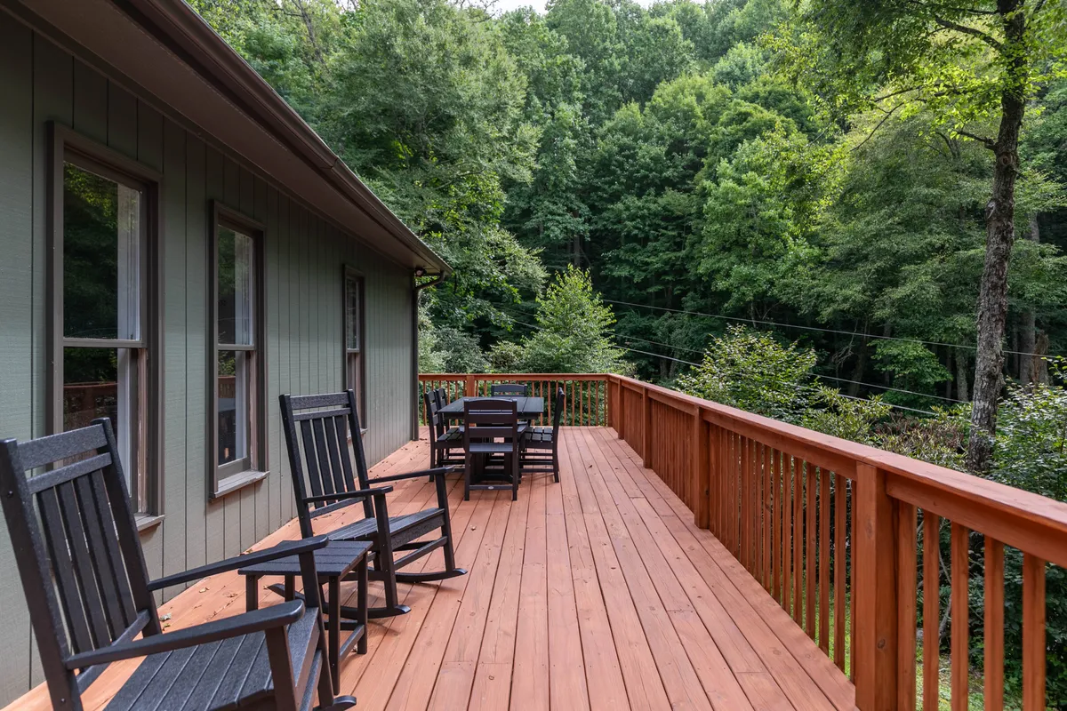 This image showcases a classic wooden deck with rocking chairs and an outdoor dining table, set against a backdrop of green trees. The deck exudes mountain charm and is perfect for enjoying morning coffee or sunset views in fresh air.