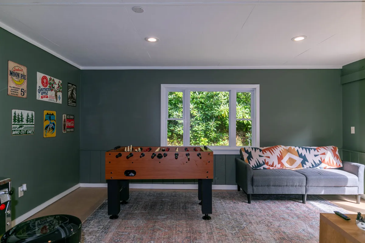 A relaxed view of the game room highlighting the foosball table, a plush sofa for spectators or relaxation, and sunlit windows that create a cheerful, inviting environment.