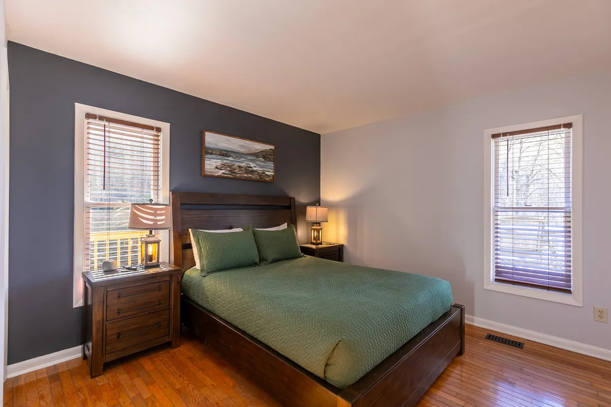 A bright, inviting bedroom featuring a plush king bed flanked by nightstands, with soft natural light filtering through a window and calming artwork on the walls. The overall atmosphere is peaceful, perfect for unwinding after a busy day.