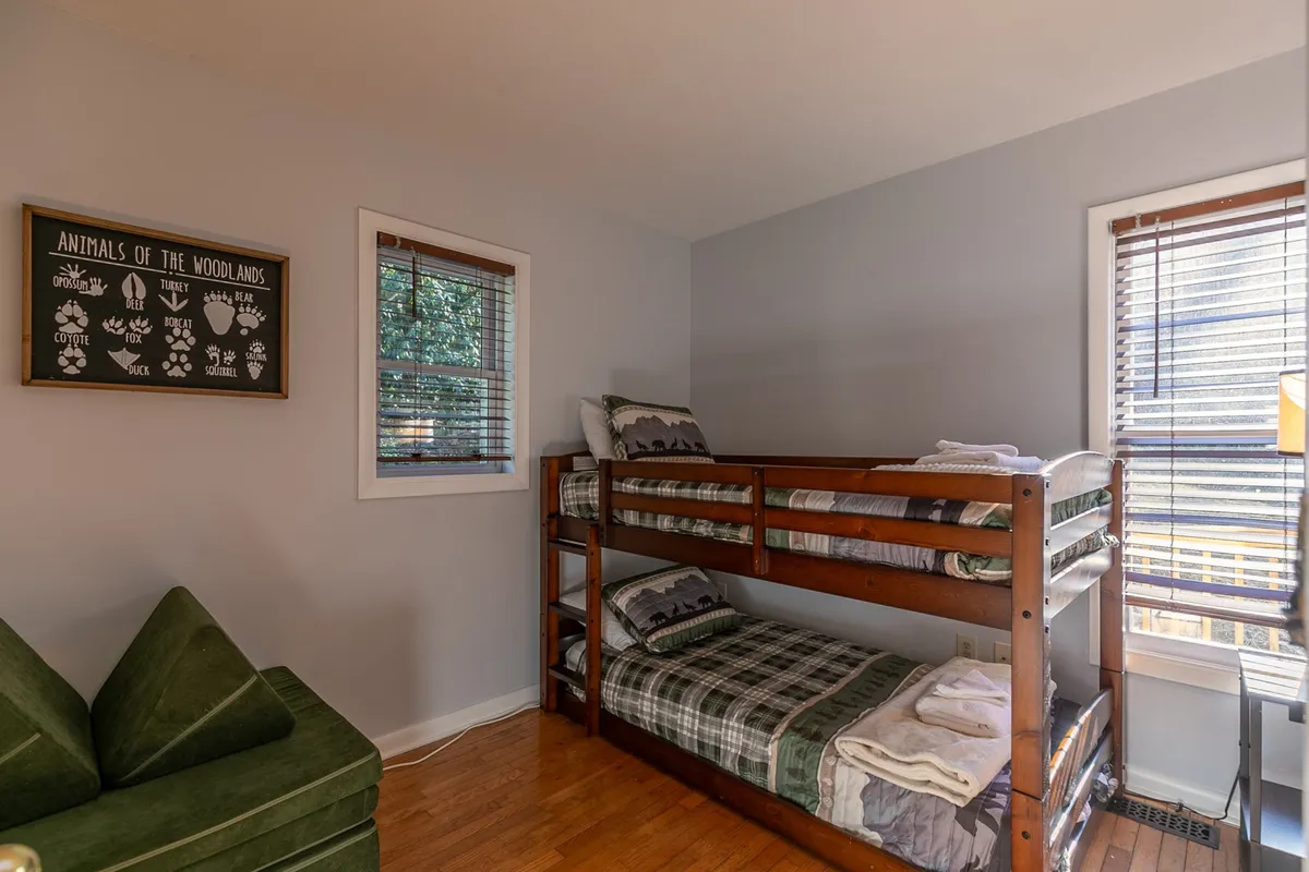 A cheerful bunk room outfitted with playful bunk beds, a green couch for lounging or reading, and rustic wooden wall art. The mood is friendly and fun, making it perfect for children or friends sharing the space.