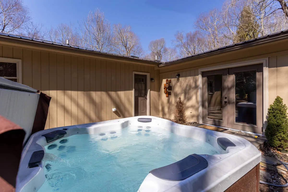 A hot tub set on the home’s exterior, framed by trees and decorative wall elements, offers a serene spot for unwinding. The easy entry and proximity to nature make it ideal for evenings of storytelling or quiet stargazing.