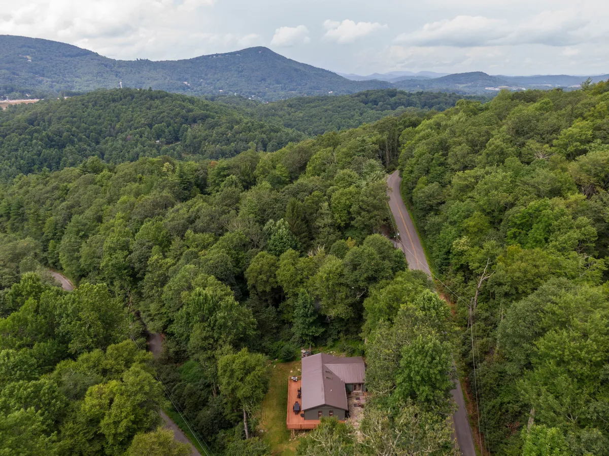 A scenic exterior view of the house nestled within a forest, with distant mountains forming a dramatic backdrop. The surrounding nature, visible from the property, hints at nearby adventures and outdoor exploration, aligning perfectly with the section's focus on Boone as a family adventure hub.