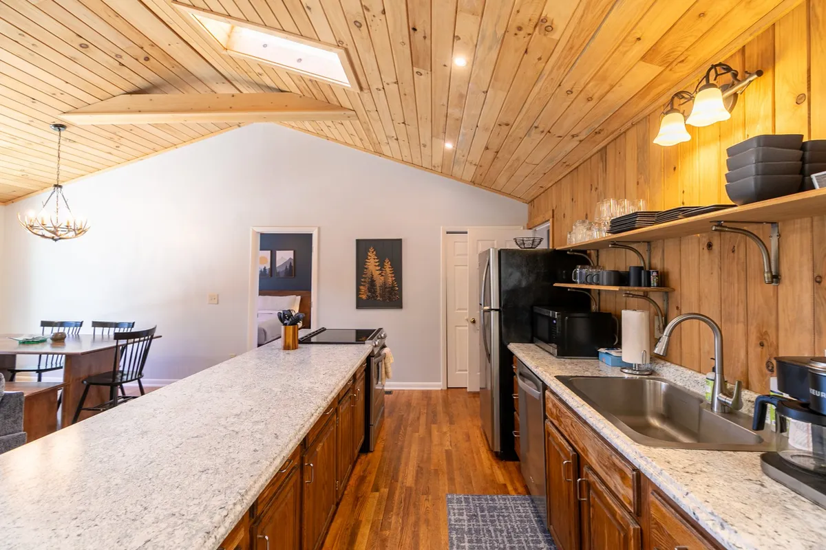 A welcoming kitchen and dining space with granite countertops, wooden cabinetry, a skylight, and a dining area. The scene suggests a bright, lively hub for brunches, casual meals, or entertaining friends throughout the year.