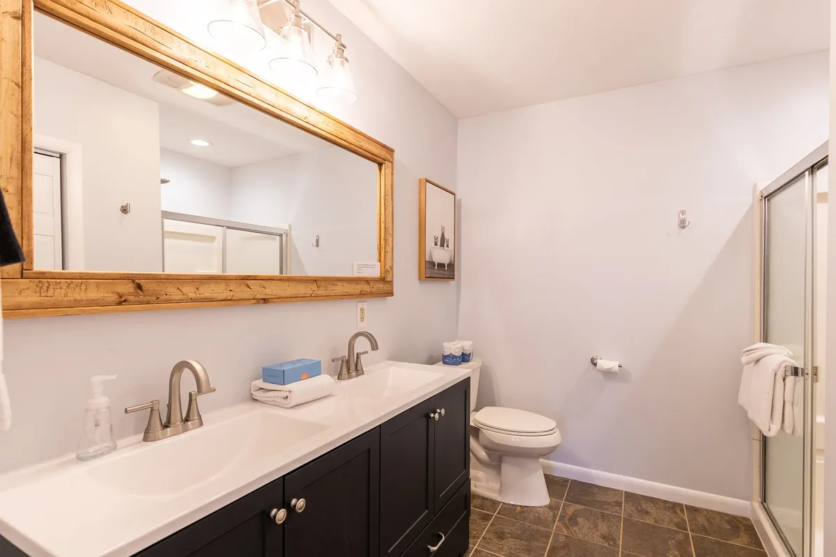 A bright, modern bathroom with a double sink vanity, a large mirror, and framed artwork. Morning sunlight brightens the space, ideal for personal grooming and relaxing routines.