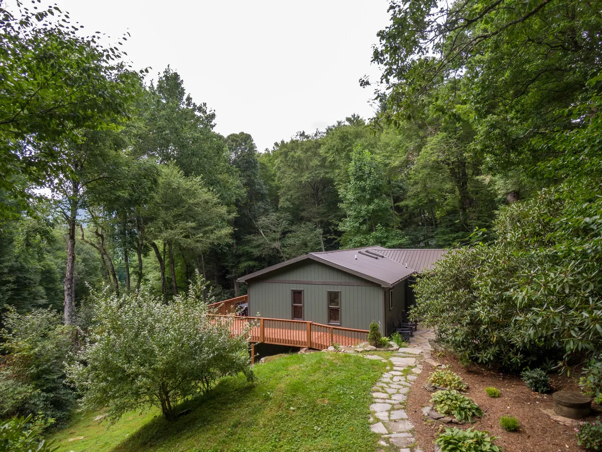 This image captures the house's exterior, highlighting the expansive wooden deck and a landscaped pathway leading to the entrance. The setting is peaceful, surrounded by lush greenery and inviting outdoor spaces perfect for gathering or quiet relaxation.