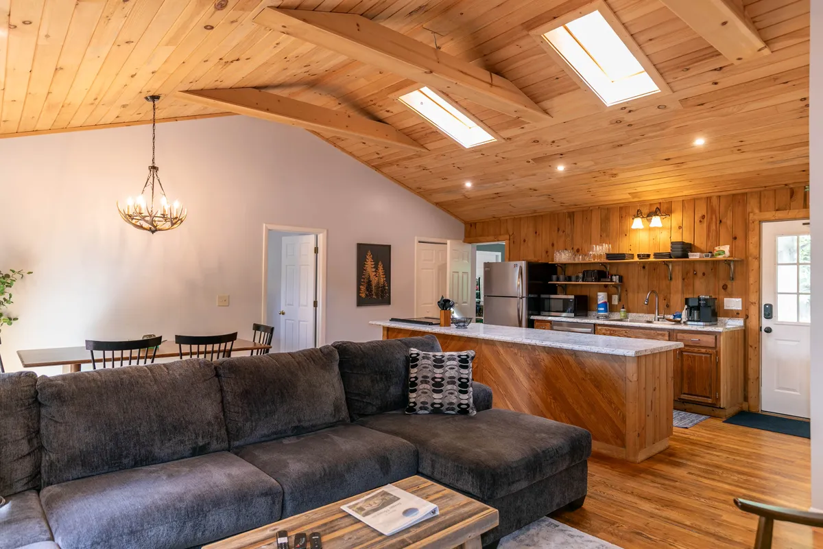 A wide view of the open-concept living area, featuring a comfortable sofa, a kitchen island, a dining table, and a sparkling chandelier overhead. The space feels warm and welcoming, perfect for relaxing after a day of outdoor adventures or gathering for family dinners.